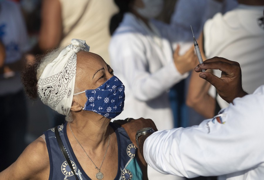 A woman wearing a mask looks at an empty syringe held by a health-care worker.