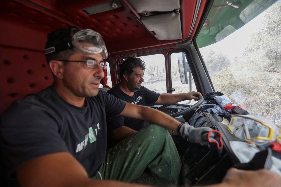 Two men sit inside the cab of a truck looking out the window.