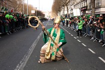 A performer dressed as as Saint Patrick poses with his staff as if it were a rock guitar, during a St. Patrick's Day parade.