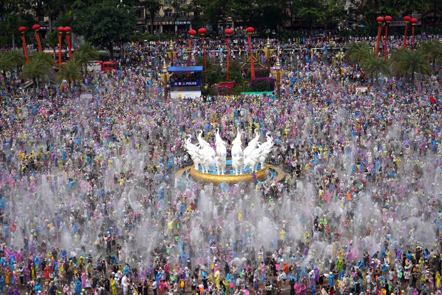A large group of people spray and throw water on each other in a square.