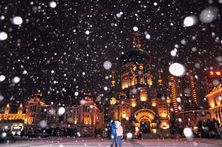 People take photos during a snowstorm at night near a cathedral.