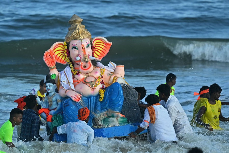 People carry a large elephant-headed idol into the surf.