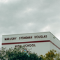 photo of building with "Marjory Stoneman Douglas High School" on it, behind trees against cloudy gray sky