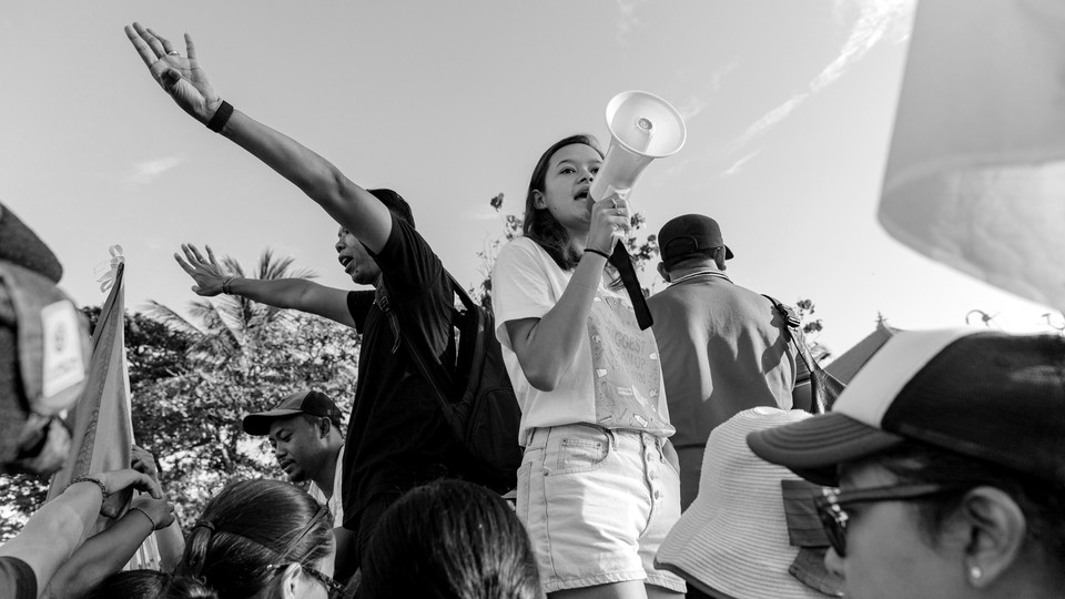 A black and white picture of a protest, focusing on a young woman with a megaphone.