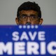 Dinesh D'Souza stands behind podium that reads: Save America. His glasses are spotted with rain.