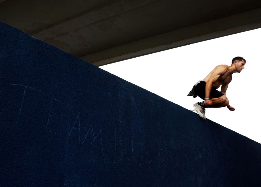 An athlete crouches as they drop from a high wall.