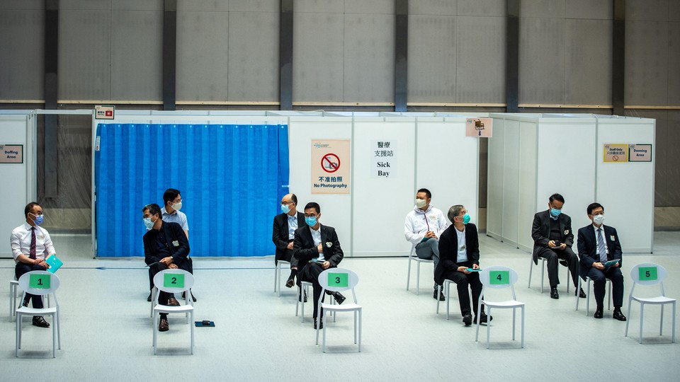 Hong Kong government officials sit in socially distanced chairs to get the second jab of the Sinovac vaccine.