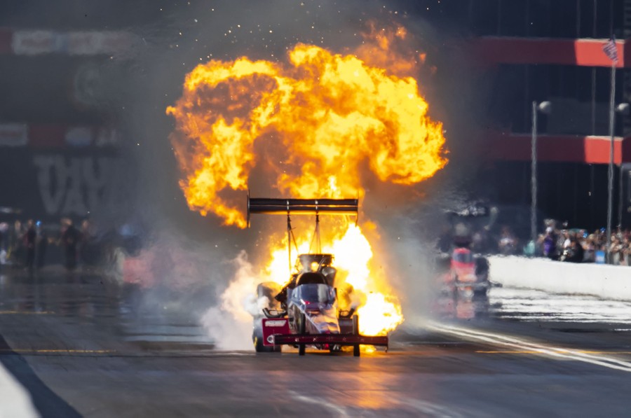Flames rise up from the rear of a dragster on a race track.