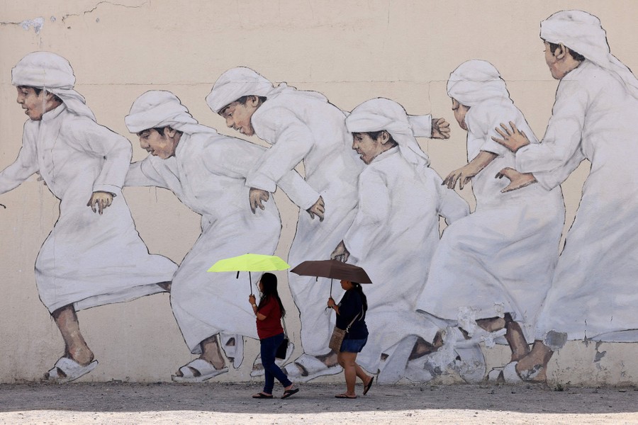 Two people walk beside a large mural depicting children running.