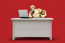 A statue of Socrates sits at a desk and ponders a laptop.