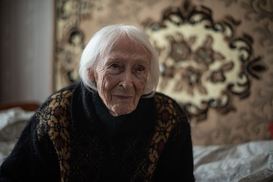 An elderly woman sits on a bed.