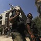 Two men with guns walk down a street in Syria.