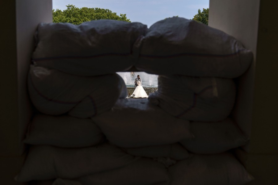 A bride and groom are captured through a hole in sandbags.