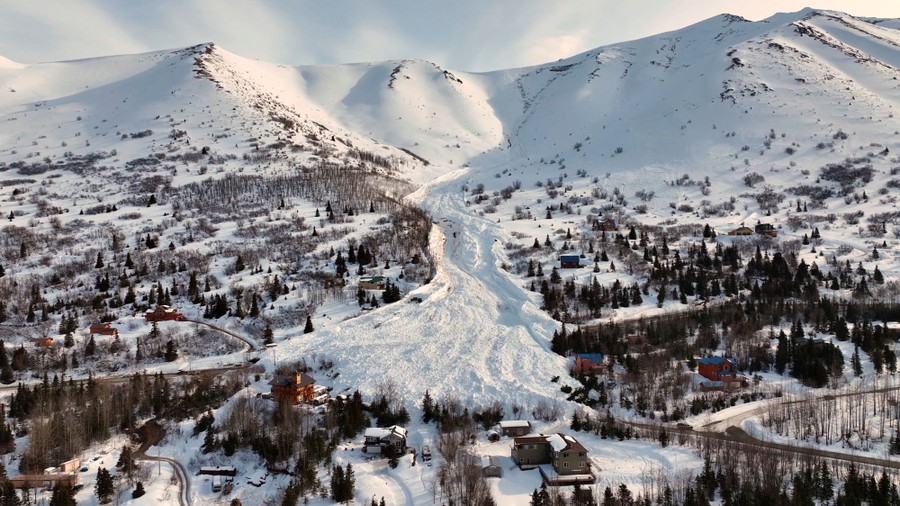An aerial view of a rural mountainside road partially covered snow from by a recent avalanche