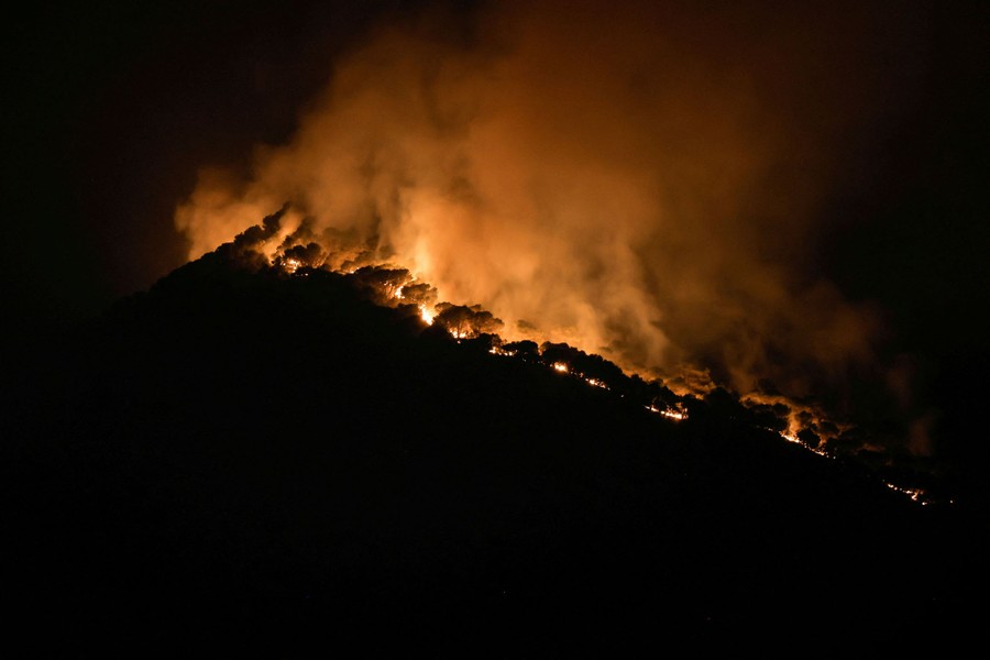 The glow of a forest fire illuminates the trees it is burning on a hillside, pictured at night.