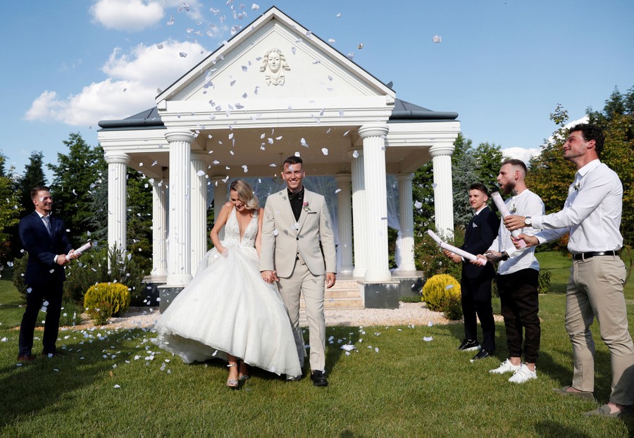 Several people launch confetti above a bride and groom during a wedding ceremony outdoors.