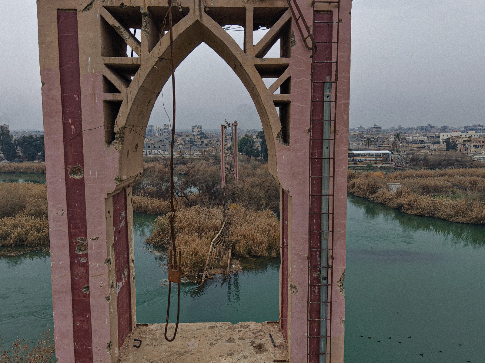 An aerial view of a war-damaged bridge, mostly collapsed, in a river in Syria.