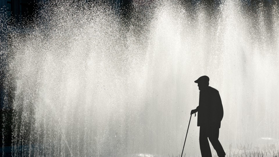 A man with a cane is silhouetted against water spraying from fountains.
