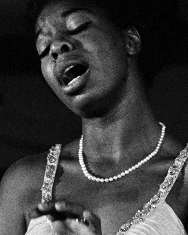 Nina Simone singing with her eyes closed, wearing a pearl necklace