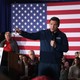A photo of Ron DeSantis standing in front of a small, seated crowd and an American flag