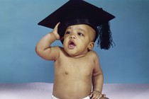 A baby clad in only a diaper holds a graduation cap on his head with an open-mouthed expression