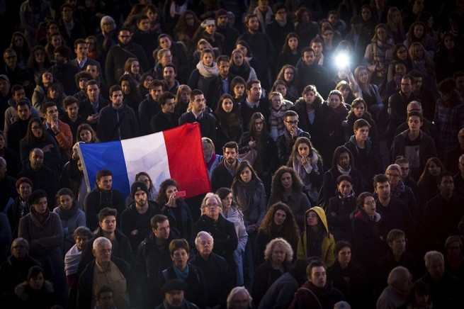 a crowd of mourners gathers outside, with some clutching a French flag