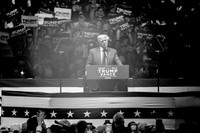 A black-and-white photo of Donald Trump standing at a podium, speaking to a crowd at Madison Square Garden.