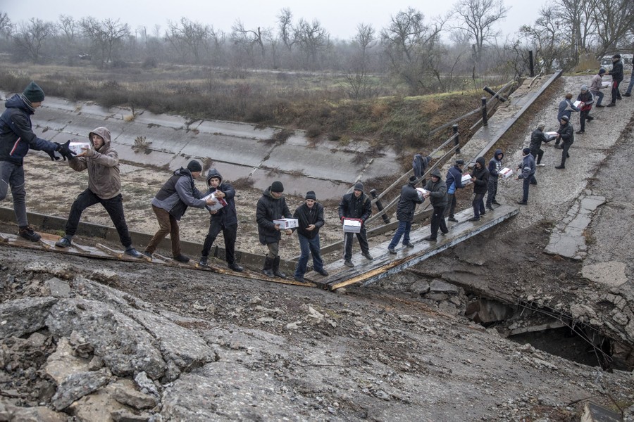 About 20 people stand in a line across a destroyed road bridge, handing one another boxes in a human chain.