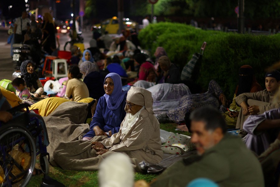 Dozens of people sit on blankets and grass in a city at night.