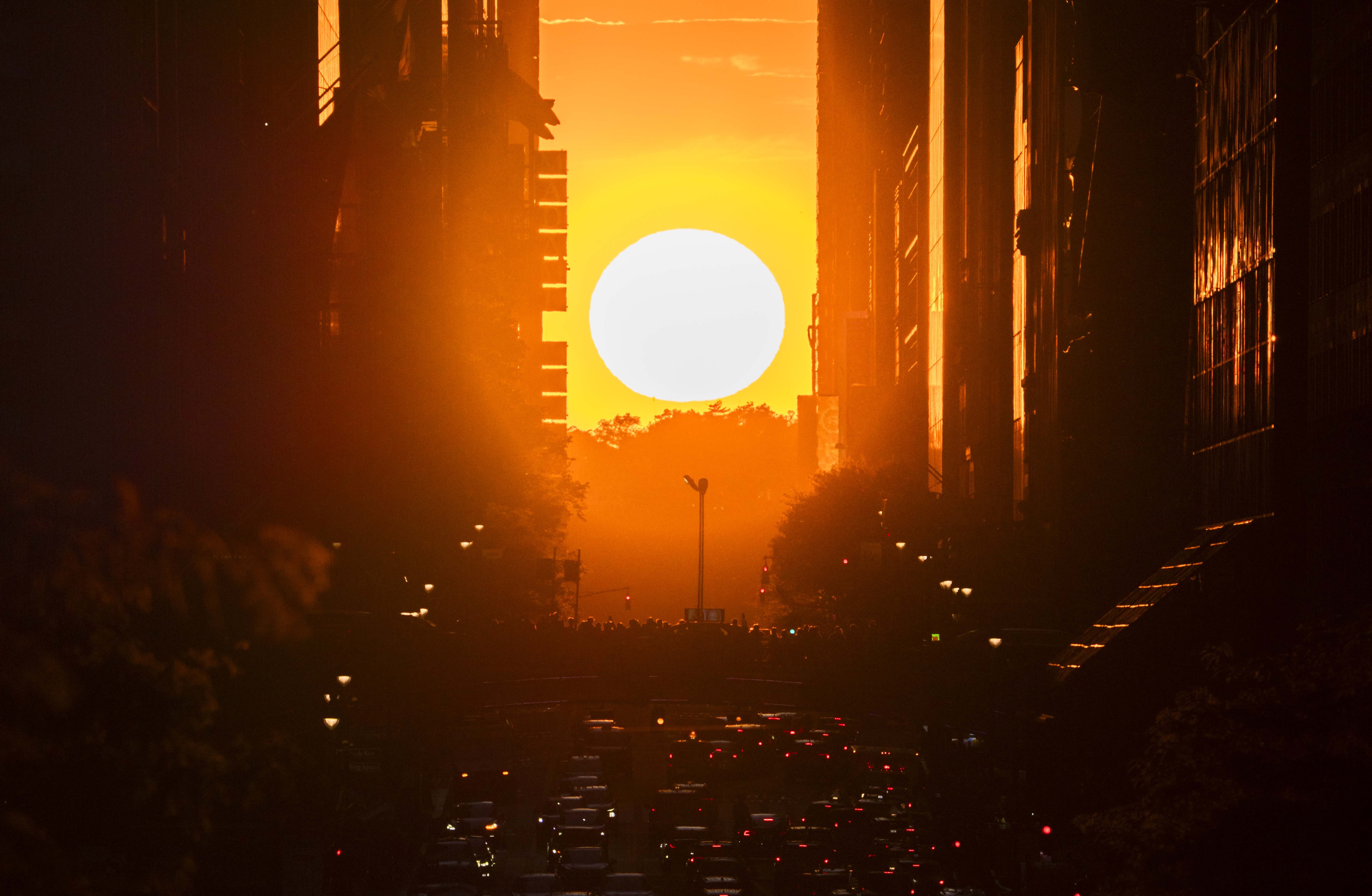 A sunset, viewed over a street between many tall buildings in New York City