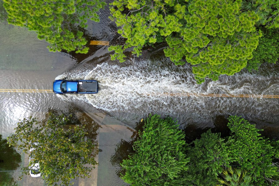A vehicle drives along a flooded street.