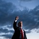 President Trump, standing, raises his fist, with a dark sky behind him