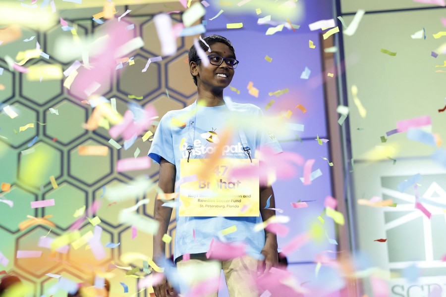 A young person smiles on a spelling-bee stage, surrounded by falling confetti.