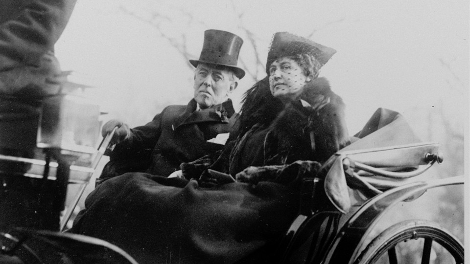 A black-and-white photo of a man in a top hat and a woman riding in a carriage