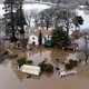 A two-story white house in California shown surrounded on all sides by muddy water halfway up its first level