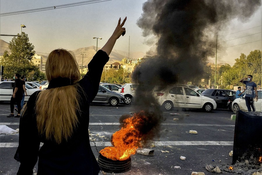 A woman stands near a burning tire in a street as part of a protest.