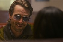 Glen Powell wearing aviator sunglasses and smiling