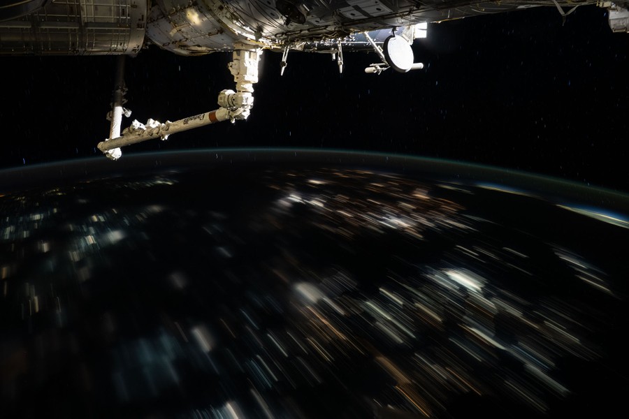 City lights streak by, below the ISS, seen at night in a long-exposure shot