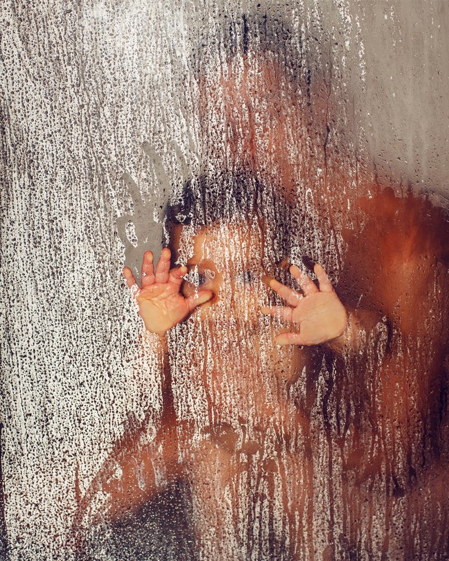 The blurry outline of a parent holding a child with their hands pressed to a glass pane covered in water droplets