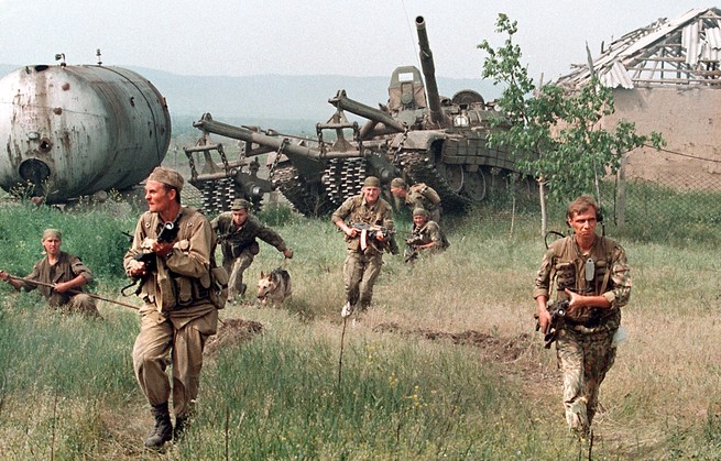 Russian soldiers advancing on a field followed by a tank.