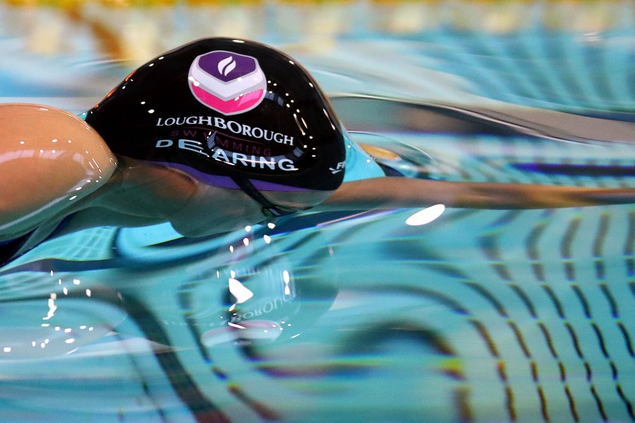 A woman swims near the surface of a pool, with the water smoothly flowing over her head and arms.