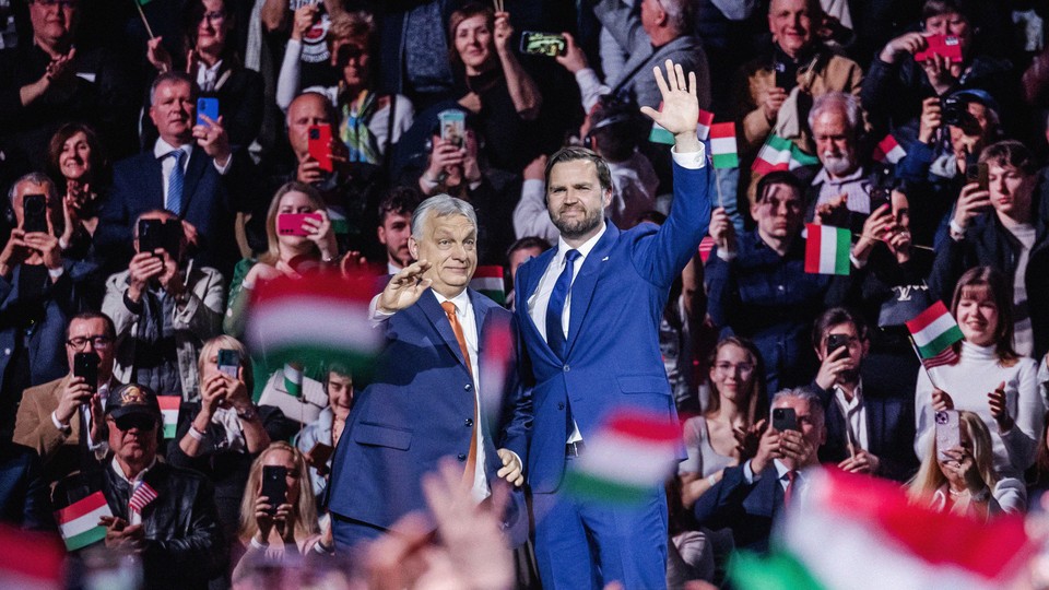 Victor Orbán stands next to J. D. Vance as both of them raise one hand to wave to the crowd.