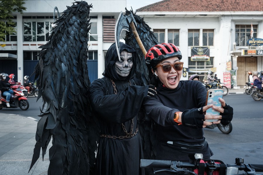 A person dressed as the Grim Reaper poses for a selfie with a cyclist in a street.