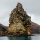 photo of large rock tower jutting from hilly shoreline with gray sky and bird