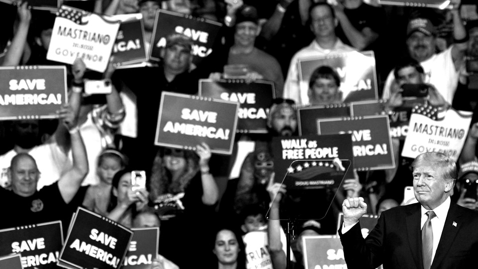 A black-and-white image of Donald Trump at a rally with supporters in the background.