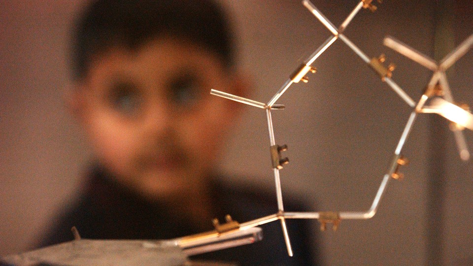 A boy stands behind a model of DNA. 