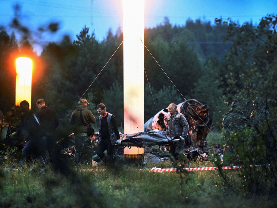 People carry a body bag near aircraft wreckage in a field.