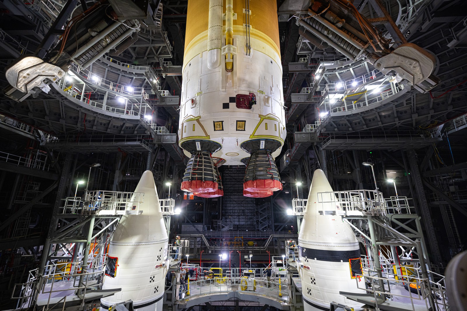 A rocket is lowered into place beside two solid rocket boosters, inside a tall building.