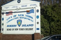 A sign reading "City of New York Correction Department: Rikers Island, Home of New York's Boldest"