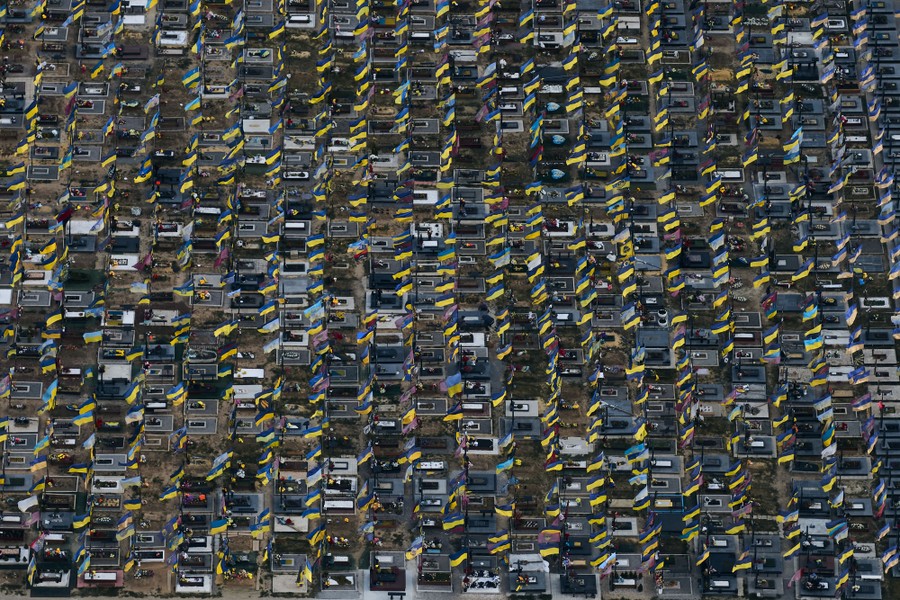 An aerial view of many gravestones in a cemetery, each adorned with a small Ukrainian flag